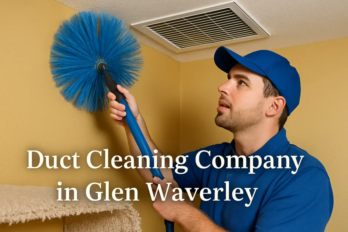 A duct cleaning technician in a blue uniform and cap uses a large blue brush to clean a ceiling vent.